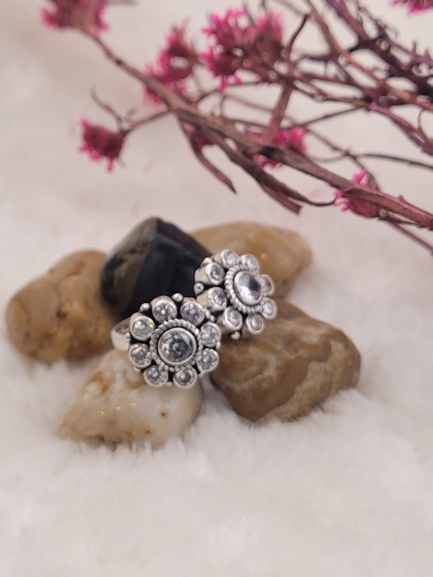 Silver toe ring with floral design on a stone surface with pink flowers in the background